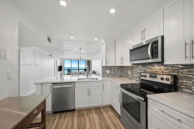 kitchen with white cabinetry, kitchen peninsula, a textured ceiling, and stainless steel appliances