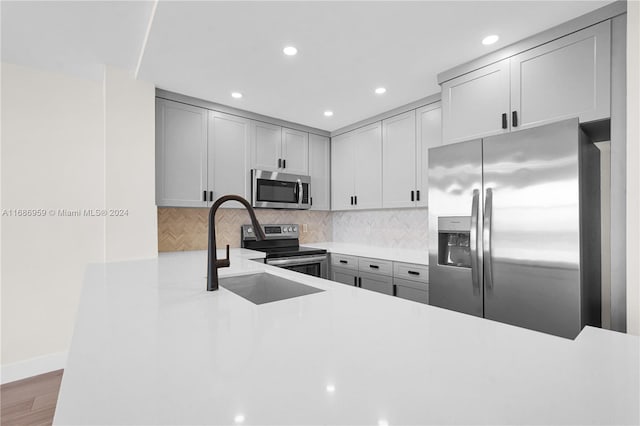 kitchen with stainless steel appliances, tasteful backsplash, gray cabinets, and hardwood / wood-style floors