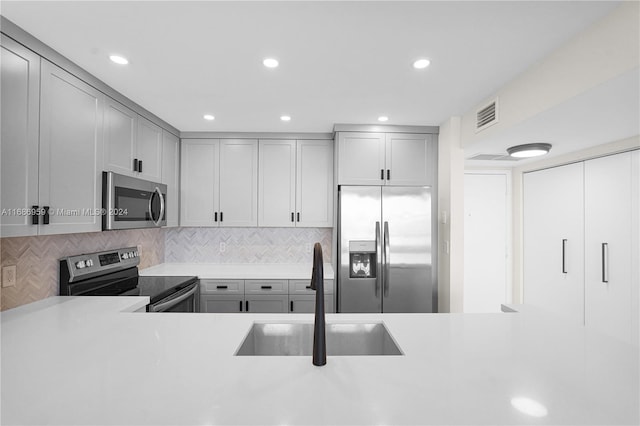 kitchen featuring gray cabinets, sink, decorative backsplash, and stainless steel appliances