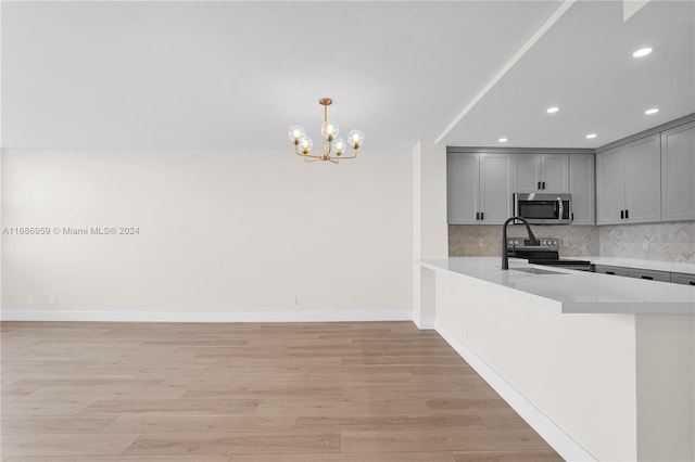 kitchen featuring kitchen peninsula, backsplash, light hardwood / wood-style flooring, gray cabinetry, and stainless steel appliances