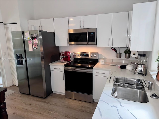 kitchen with light stone countertops, appliances with stainless steel finishes, sink, hardwood / wood-style floors, and white cabinetry