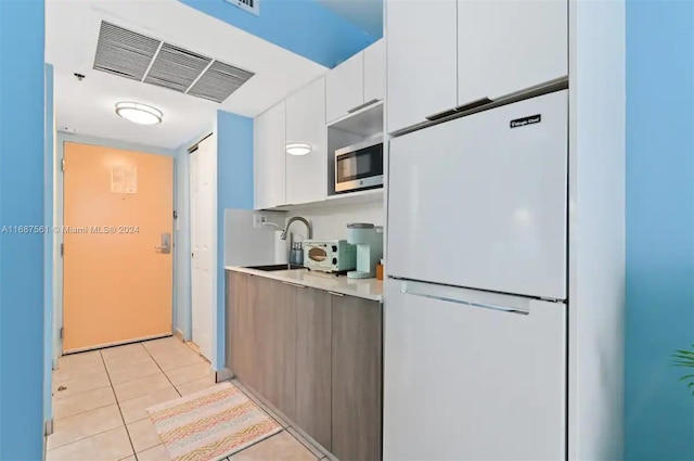 kitchen with light tile patterned flooring, stainless steel microwave, sink, white cabinetry, and white fridge