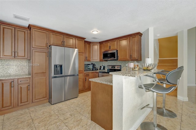 kitchen featuring kitchen peninsula, stainless steel appliances, light stone counters, and backsplash