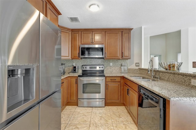 kitchen with kitchen peninsula, appliances with stainless steel finishes, sink, and light stone countertops