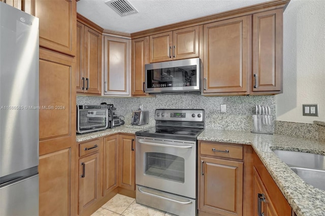 kitchen featuring light stone counters, a textured ceiling, tasteful backsplash, light tile patterned floors, and appliances with stainless steel finishes