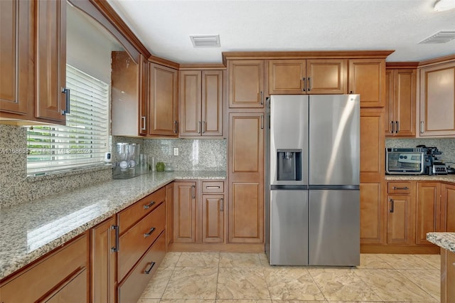 kitchen featuring decorative backsplash, stainless steel refrigerator with ice dispenser, a textured ceiling, and light stone counters