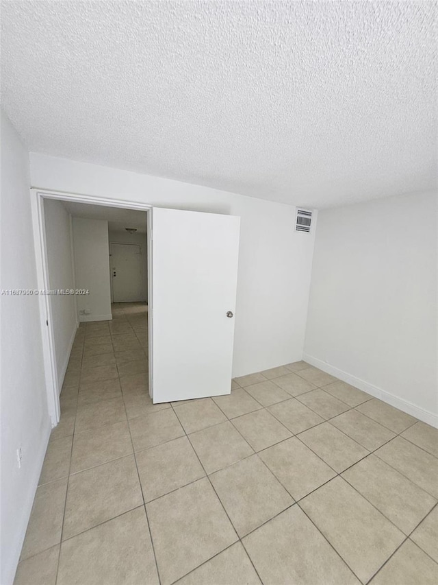 empty room featuring a textured ceiling and light tile patterned floors