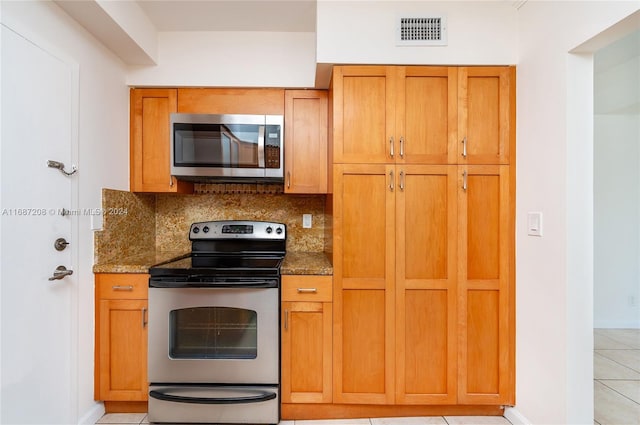 kitchen with appliances with stainless steel finishes, dark stone countertops, light tile patterned flooring, and backsplash