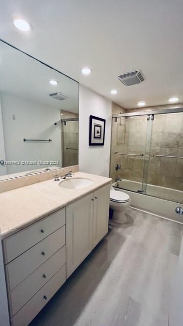 full bathroom featuring vanity, hardwood / wood-style floors, combined bath / shower with glass door, and toilet