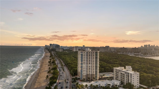 aerial view at dusk featuring a water view and a view of the beach