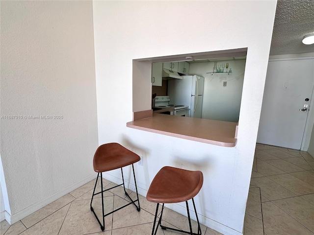 kitchen featuring a breakfast bar area, a textured ceiling, white appliances, and light tile patterned floors