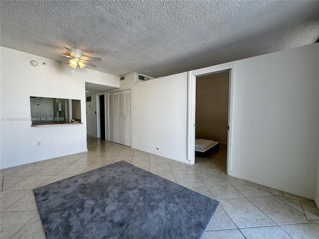 empty room with a textured ceiling, ceiling fan, and light tile patterned flooring