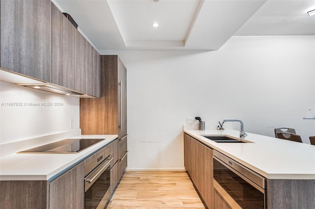 kitchen with oven, beverage cooler, light wood-type flooring, black electric stovetop, and sink