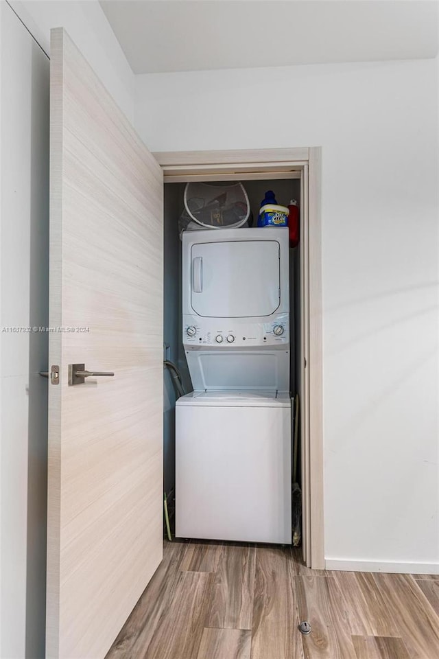 laundry room with stacked washer and clothes dryer and hardwood / wood-style flooring