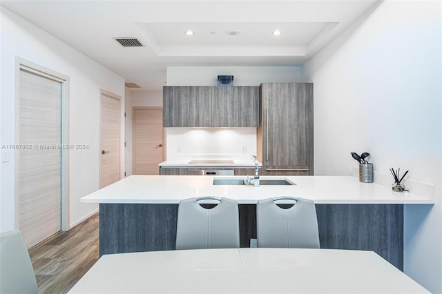 kitchen featuring kitchen peninsula, sink, a tray ceiling, and light wood-type flooring