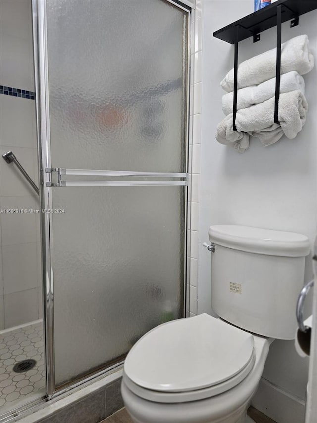 bathroom with a shower with shower door, toilet, and tile patterned flooring