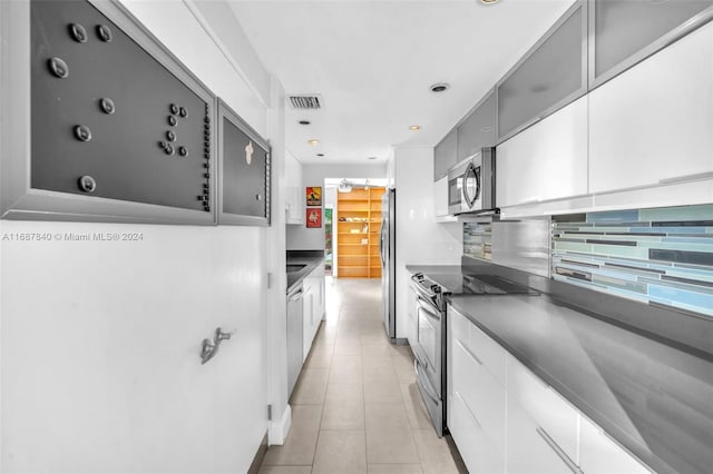 kitchen with gray cabinetry, light tile patterned flooring, stainless steel appliances, white cabinets, and decorative backsplash