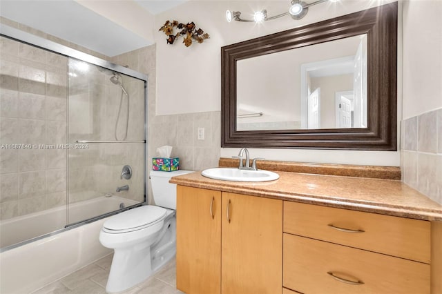 full bathroom with bath / shower combo with glass door, tile walls, toilet, vanity, and tile patterned flooring