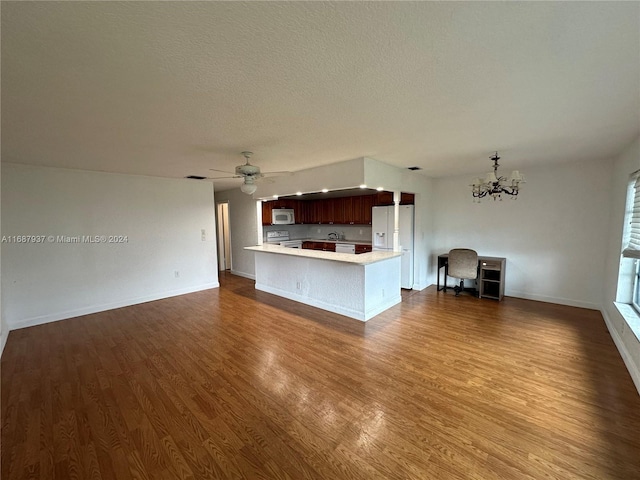 kitchen featuring ceiling fan with notable chandelier, dark wood-type flooring, kitchen peninsula, a textured ceiling, and white appliances