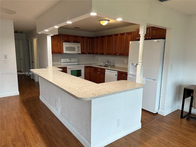 kitchen with dark wood-type flooring, kitchen peninsula, white appliances, and sink