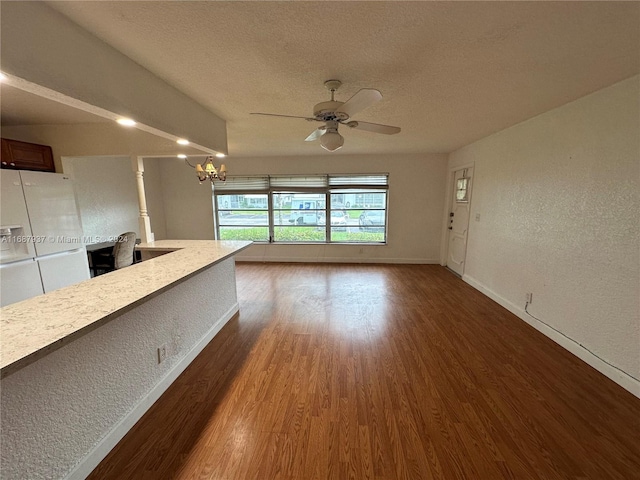 unfurnished living room with ceiling fan with notable chandelier, dark wood-type flooring, and a textured ceiling