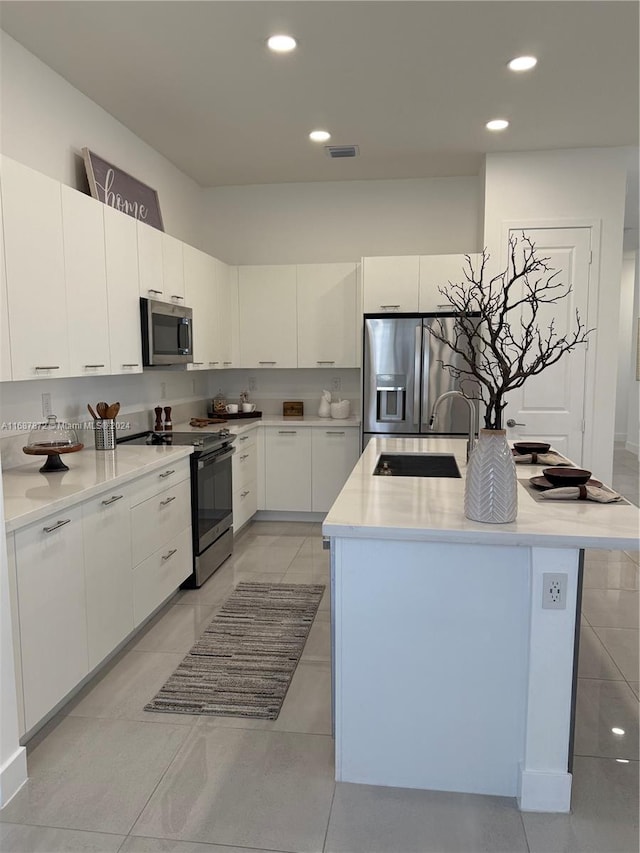 kitchen with white cabinets, appliances with stainless steel finishes, sink, and a kitchen island with sink