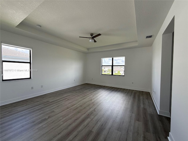 empty room with ceiling fan, a textured ceiling, a tray ceiling, and dark hardwood / wood-style floors