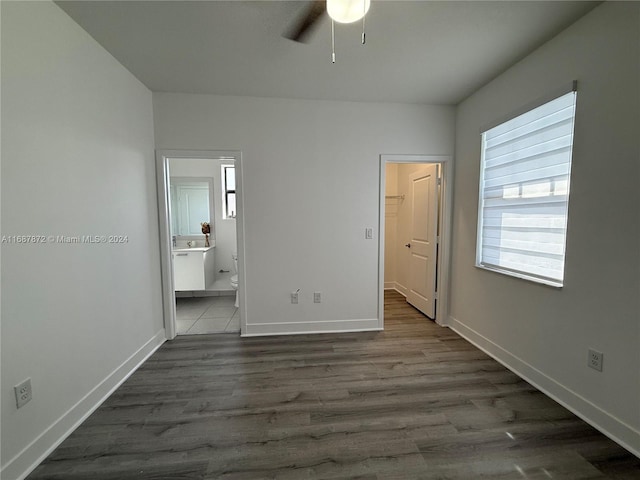 unfurnished bedroom featuring a spacious closet, ensuite bath, dark hardwood / wood-style flooring, and ceiling fan