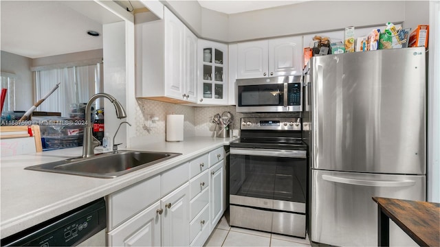 kitchen featuring appliances with stainless steel finishes, sink, white cabinets, decorative backsplash, and light tile patterned floors