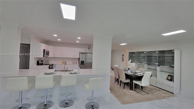 kitchen with appliances with stainless steel finishes, sink, kitchen peninsula, white cabinets, and a breakfast bar area