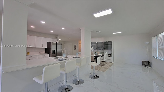 kitchen with sink, kitchen peninsula, a breakfast bar area, white cabinetry, and stainless steel fridge with ice dispenser