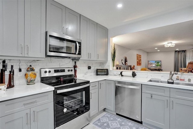 kitchen with stainless steel appliances, sink, kitchen peninsula, gray cabinets, and decorative backsplash