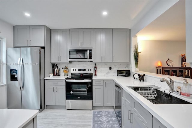 kitchen featuring appliances with stainless steel finishes, gray cabinets, decorative backsplash, sink, and light hardwood / wood-style flooring