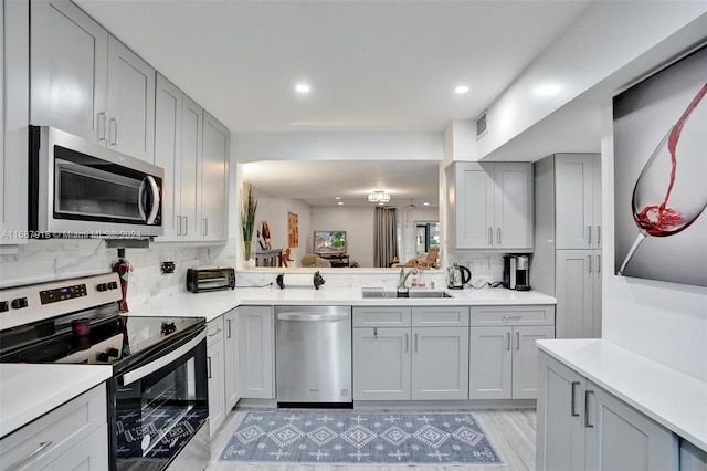 kitchen featuring stainless steel appliances, light hardwood / wood-style floors, sink, gray cabinets, and decorative backsplash