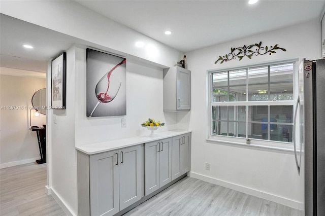 bar with light hardwood / wood-style flooring, gray cabinetry, and stainless steel fridge