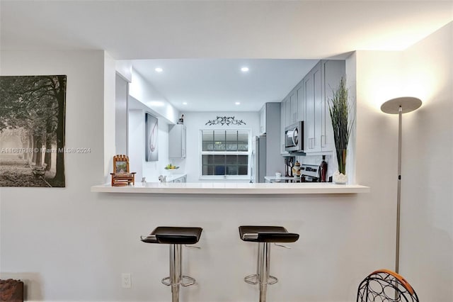 kitchen featuring kitchen peninsula, gray cabinetry, a breakfast bar, and appliances with stainless steel finishes