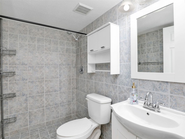 bathroom with toilet, tile walls, a textured ceiling, a tile shower, and vanity