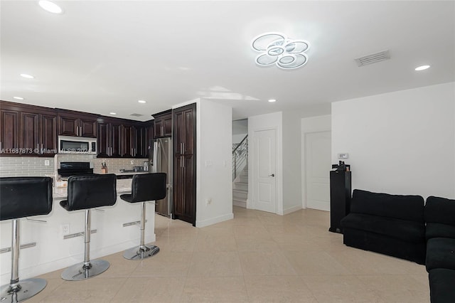 kitchen featuring a kitchen breakfast bar, decorative backsplash, appliances with stainless steel finishes, dark brown cabinets, and a kitchen island