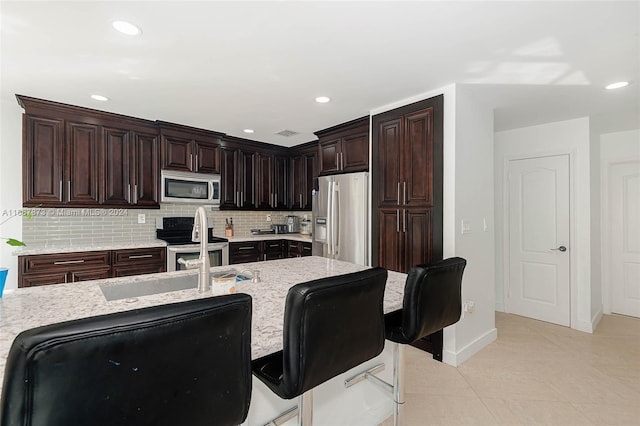 kitchen with backsplash, a kitchen breakfast bar, light tile patterned floors, dark brown cabinetry, and stainless steel appliances