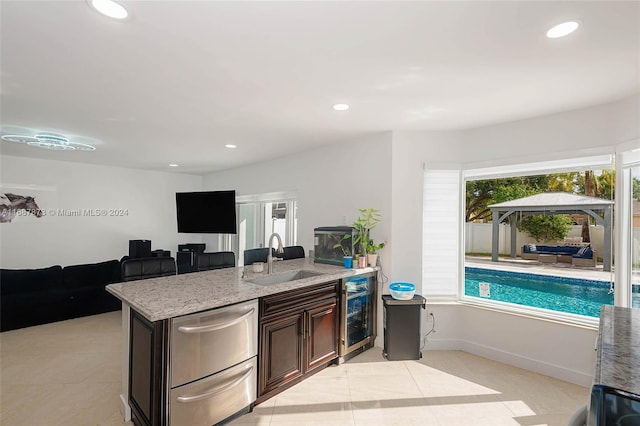 kitchen with wine cooler, light stone countertops, sink, and dark brown cabinets