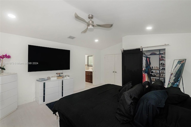 carpeted bedroom with a barn door, ensuite bathroom, vaulted ceiling, and ceiling fan