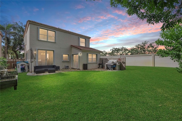 back house at dusk featuring outdoor lounge area, cooling unit, a lawn, and a patio area