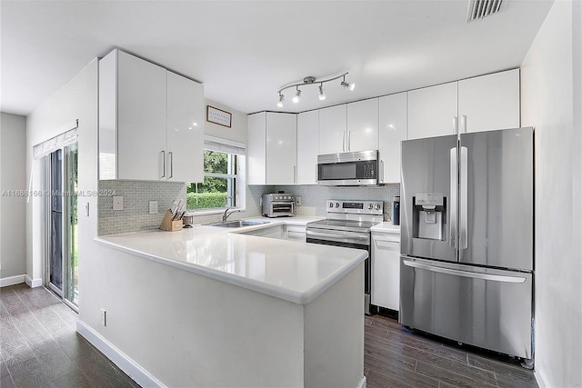 kitchen with stainless steel appliances, dark hardwood / wood-style flooring, kitchen peninsula, sink, and white cabinetry