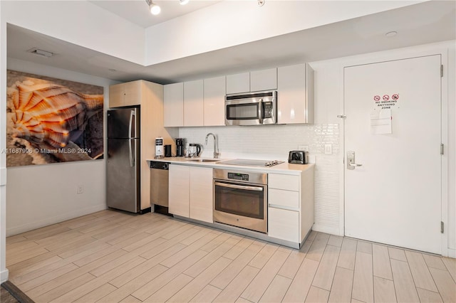 kitchen featuring decorative backsplash, white cabinetry, sink, light hardwood / wood-style floors, and stainless steel appliances