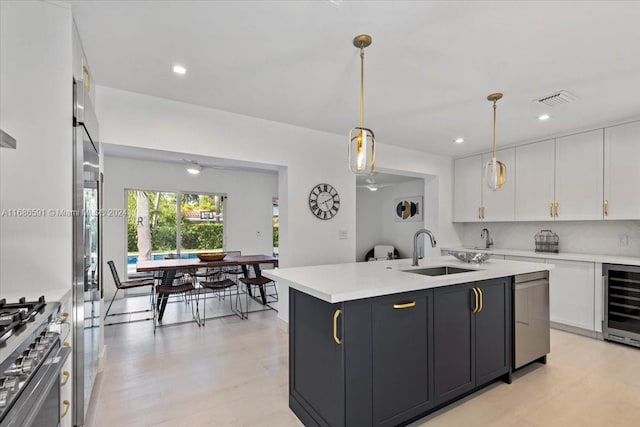 kitchen with white cabinetry, sink, stainless steel appliances, beverage cooler, and an island with sink