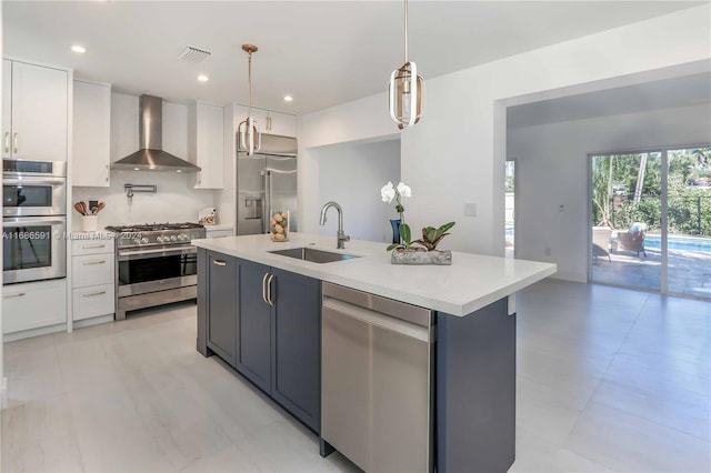 kitchen with high quality appliances, a kitchen island with sink, sink, wall chimney exhaust hood, and white cabinetry