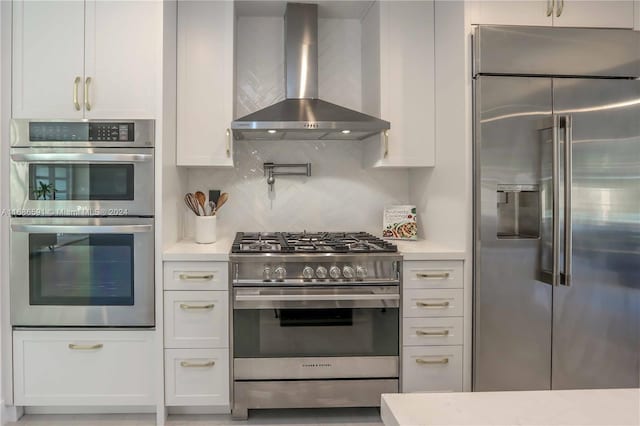 kitchen featuring white cabinets, premium appliances, decorative backsplash, and wall chimney range hood