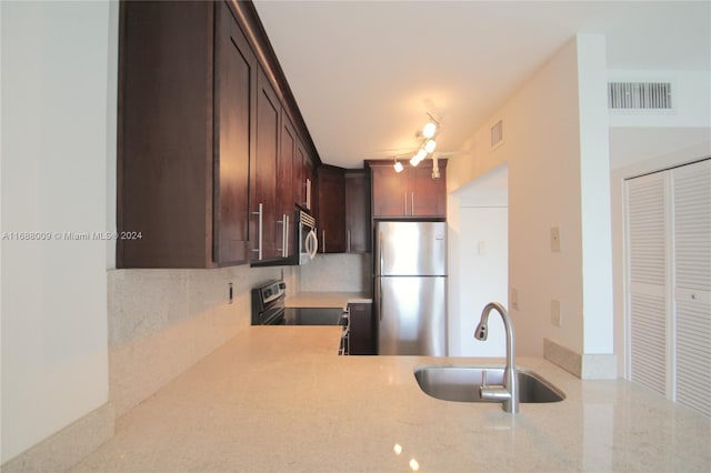 kitchen with dark brown cabinetry, sink, appliances with stainless steel finishes, tasteful backsplash, and light stone countertops