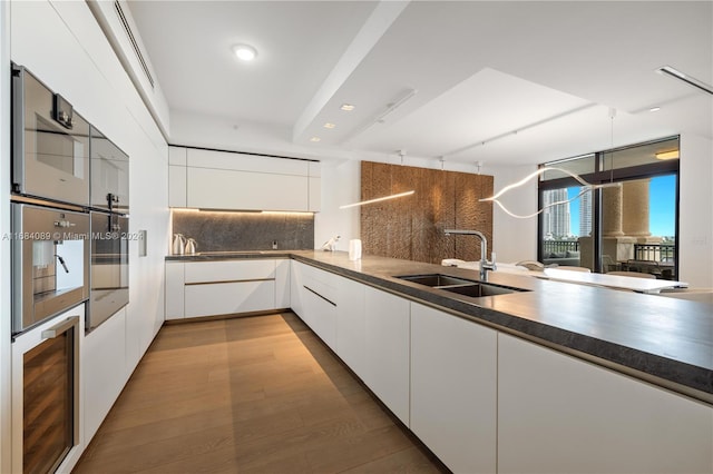 kitchen featuring wine cooler, sink, tasteful backsplash, white cabinets, and light wood-type flooring