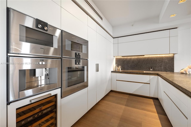 kitchen with light wood-type flooring, stainless steel double oven, beverage cooler, and white cabinets